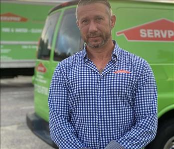 SERVPRO male employee standing in front of green trucks